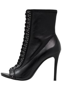 Stivale alla caviglia in pelle nera con punta aperta e tacco a stiletto. Presenta una chiusura con lacci sul davanti e borchie decorative lungo il lato, con una texture liscia.