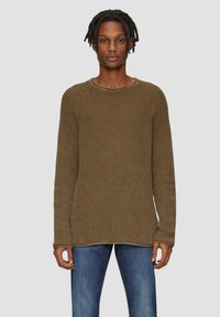 Pull en tricot marron avec un motif texturé, col rond et manches longues, associé à un jean bleu. Design simple et coupe décontractée.