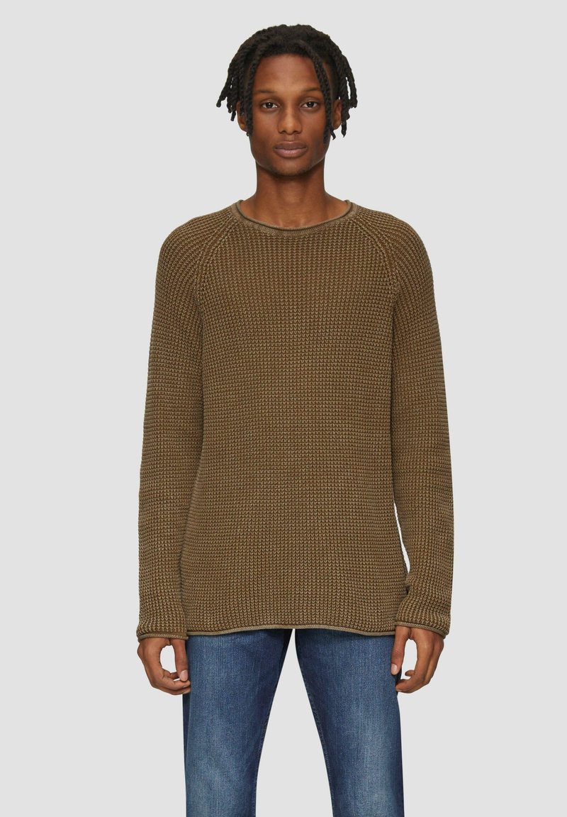 Pull en tricot marron avec un motif texturé, col rond et manches longues, associé à un jean bleu. Design simple et coupe décontractée.
