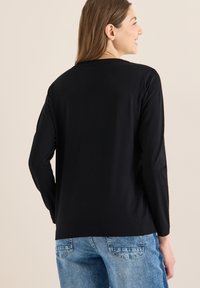 Černé tričko s dlouhým rukávem a kulatým výstřihem, hladké textury a volného střihu, doplněné světlými modrými džínami.