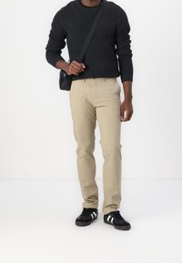 Czarny sweter z dzianiny, beżowe spodnie o prostych nogawkach oraz czarne trampki z białymi paskami. Stylizację dopełnia mała czarna torebka na ramię.