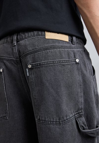 Donkergrijze denim broeken met een gestructureerde afwerking, voorzien van achterzakken, zilver hardware en een beige leren label op de tailleband.
