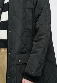 Czarna pikowana kurtka z zapięciem na zatrzaski, kieszenią naszywaną i ściągaczami z dzianiny przy mankietach. Materiał o fakturze z wzorem diamentowym.