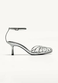 Silver strappy höga klacksandaler med ankelrem, med en smal klack och en elegant, metallisk finish, öppen tå och utskärningsdesign.