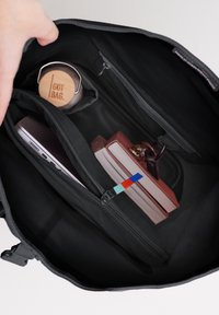 Svart väskas insida som visar en bärbar dator, böcker och en trävattenflaska med engraveringen "GOT BAG". Har flera zippered fack.