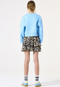Sudadera de color azul claro con un diseño corto, combinada con una falda de volantes con estampado de leopardo beige y negro. Zapatillas con detalles azules y calcetines blancos.