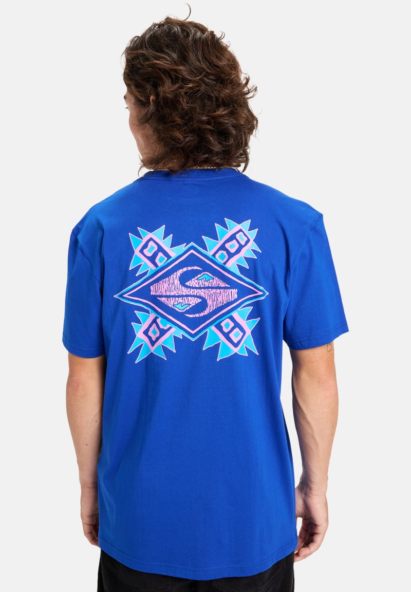 Blauwe katoenen t-shirt met een grote geometrische grafiek in roze en turkoois op de achterkant, met hoekige accenten en een ontspannen pasvorm.