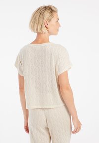 Top corto a maniche corte di colore beige con un motivo a rombi di texture. Tessuto a maglia morbido con una vestibilità ampia e scollo rotondo.