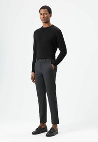 Schwarzes Langarmshirt, graue, maßgeschneiderte Hose und schwarze Slipper. Schmaler Schnitt, glatte Textur, minimalistisches Design, mit Seitentaschen und Gürtelschlaufen.