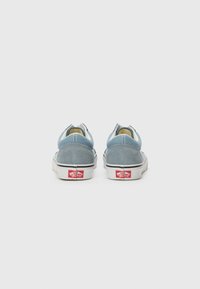 Blaue Wildleder-Sneaker mit niedrigem Profil, weißer Gummisohle und kontrastierendem roten Logo an der Ferse. Leichter Stofffutter sichtbar am Öffnungsrand.