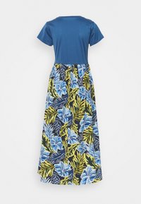 Haut bleu à manches courtes attaché à une longue jupe avec un motif floral tropical en bleu, jaune et vert sur fond sombre.