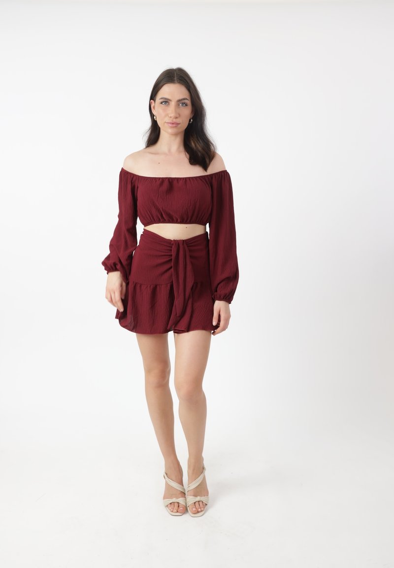 Bordeaux to-delt sæt bestående af en off-the-shoulder crop top og en højtaljet nederdel med knyttet frontdetalje og volangkant.