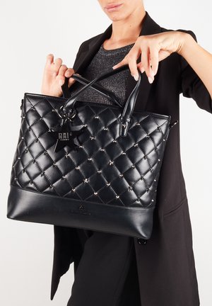 Torebka tote z pikowanej czarnej skóry z srebrnymi ćwiekami, podwójnymi uchwytami i zawieszką w kształcie gwiazdy. Charakteryzuje się gładką dolną częścią oraz usztywnioną konstrukcją.