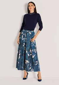 Navy trui met lange mouwen, gecombineerd met een geplooide rok tot de enkel met een blauw bloemenpatroon. Draag met donkerblauwe hakken.