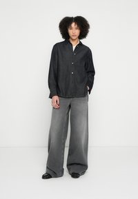 Σκούρο τζιν πουκάμισο με κουμπιά, συνδυασμένο με παντελόνι γκρι φαρδιάς γραμμής. Και τα δύο κομμάτια έχουν χαλαρή εφαρμογή και απλή λεπτομέρεια.