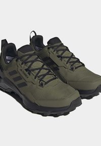 Zelené outdoorové boty z umělého materiálu; mají černé tkaničky, strukturovaný svršek a robustní černou podrážku s protiskluzovým vzorem.