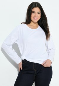 Witte langek mouwen t-shirt met een knoopdetail aan de voorkant, gecombineerd met donkere spijkerbroeken. Zacht katoenmateriaal met een relaxte pasvorm.