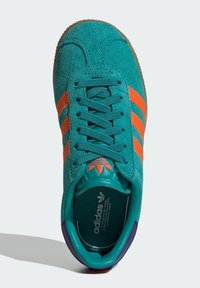 Turquoise suede sneaker with orange three-stripe design, rubber outsole, and turquoise lining. Adjustable laces and padded collar detail.