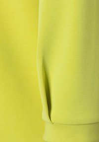 Gros plan d'un poignet de manche sur une chemise à manches longues jaune-vert vif avec texture visible du tissu et détails des coutures.