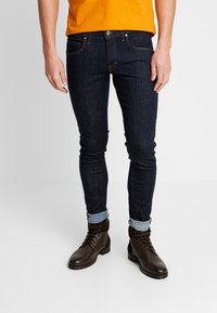 Mörka jeans med slim fit, som har en klassisk femfickdesign och uppvikta ben, i kombination med bruna snörstövlar.