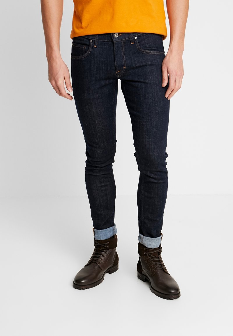 Mörka jeans med slim fit, som har en klassisk femfickdesign och uppvikta ben, i kombination med bruna snörstövlar.