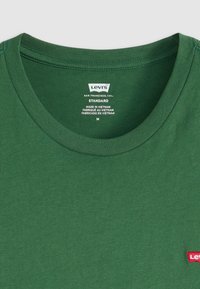 Tricou verde Levi's cu guler rotund, având un etichetă roșie cu logo, realizat din bumbac, cu o textură netedă și o croială standard. Eticheta de îngrijire este vizibilă.