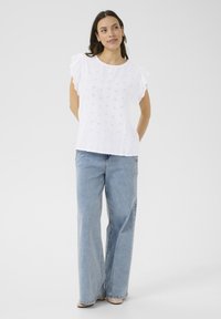 Blouse en coton blanc avec des détails en œillets, des manches volantes et un col rond, assortie à un jean large bleu clair.