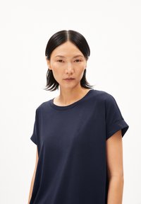 Marineblauwe katoenen t-shirt met korte opgerolde mouwen, ronde halslijn en een klein geborduurd detail op de borst. Gladde textuur.