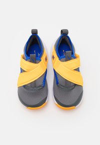 Šedé a modré sportovní boty s žlutými pásky, vybavené prodyšným svrškem, polstrovaným límcem a bílou podrážkou. Logo Nike je zobrazeno na pásech.