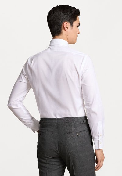 Chemise blanche à manches longues avec un col classique, associée à un pantalon gris ajusté avec des réglages latéraux et des poches arrière.