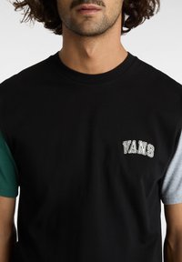 Svart t-shirt med gröna och grå ärmar. Har en liten, vit broderad "VANS"-logotyp på bröstet. Tillverkad av bomull. Avslappnad passform.