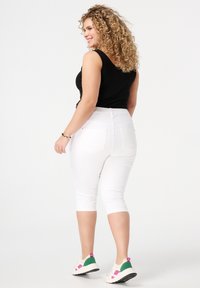 Pantalons capri blancs au design ajusté et à taille élastique, associés à un haut sans manches noir et des chaussures de sport multicolores.