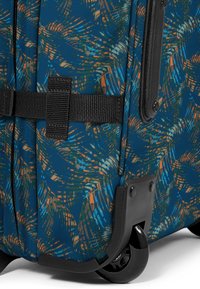 Maleta rígida con una base azul, que presenta un patrón de hojas de palma en naranja y verde. Incluye herrajes negros y ruedas que se deslizan suavemente.