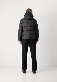 Zwarte gevoerde jas met capuchon, met horizontale stiksels, glanzend materiaal en een klein logo bij de nek. Gekocht met zwarte broeken en laarzen.