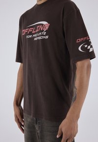 Brun kortærmet T-shirt med hvid og pink tekst "OFFLINE FOR PRIVATE REASONS" og et logo på venstre ærme. Blød bomuldsstruktur.