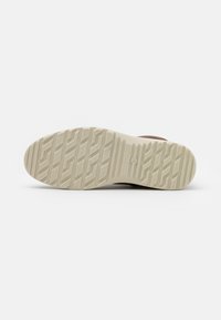 Shoe bottom with a textured, cream-colored rubber sole featuring a zigzag pattern; brown upper material visible at the edges.