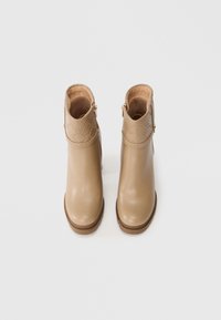 Bottines beige en matériau synthétique lisse, avec un revers à motifs, une fermeture éclair sur le côté et une semelle plate basse couleur tan.