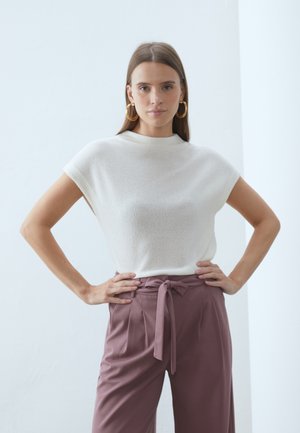 Short-sleeve, ribbed white top with a high neckline paired with high-waisted, light purple pants featuring a tied waist detail.
