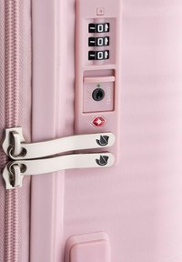 Valigia rosa chiaro con zip argentate, un lucchetto TSA e un combinatore a tre cifre. Texture liscia e design elegante.