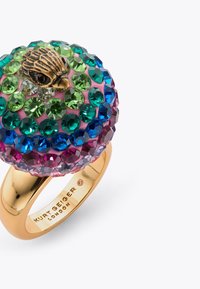 Złota obrączka z okrągłą górą ozdobioną wielokolorowymi kryształami w odcieniach zieleni, niebieskiego i różowego, z dekoracyjnym akcentem ptaka.
