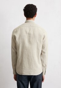 Chemise beige clair à manches longues en tissu texturé, dotée d'un col classique, de poignets boutonnés et d'un ourlet droit.