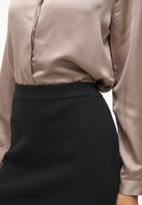 Sateng taupe-bluse med knaplukning og lange ærmer, parret med en sort ribbet strik blyantnederdel med høj talje.