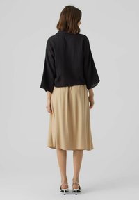 Schwarzes, strukturiertes Oberteil mit weit geschnittenen Ärmeln, kombiniert mit einem fließenden beigefarbenen Midirock. Das Outfit zeichnet sich durch ein einfaches Design ohne sichtbare Muster aus.