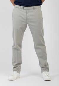 Chino grigio chiaro realizzati in morbido cotone. Presentano una chiusura con bottone frontale, tasche laterali e un design con gamba affusolata. Indossati con sneaker bianche.