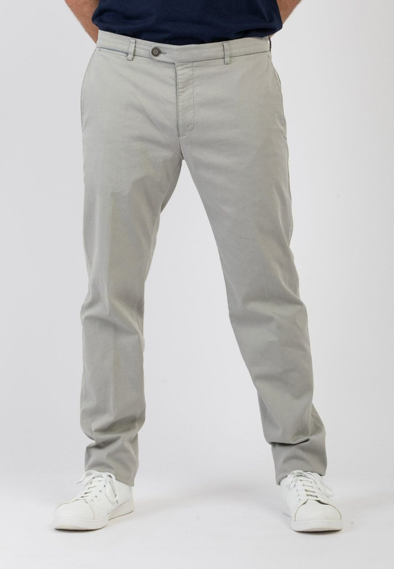 Chino grigio chiaro realizzati in morbido cotone. Presentano una chiusura con bottone frontale, tasche laterali e un design con gamba affusolata. Indossati con sneaker bianche.