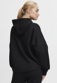 Felpa nera oversize con cappuccio regolabile, maniche larghe e orlo a coste. Texture liscia, design minimalista, adatta per un abbigliamento casual.
