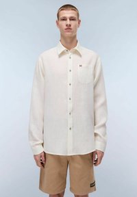 Camicia a maniche lunghe color beige chiaro, realizzata in lino, con un abbottonatura sul davanti, una tasca sul petto e un piccolo dettaglio a bandiera sulla tasca.