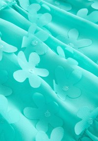 Türkiis värvi kangas, millel on kerge tekstuur, kujundatud poolläbipaistvate lillemustrite ja ümmarguste aktsentidega kogu pinna ulatuses.