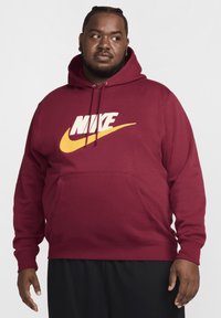 Sudadera burdeos con capucha, que presenta un gran logo de Nike en blanco y un swoosh amarillo. Fabricada con un tejido suave y cuenta con un bolsillo frontal.