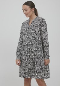 Schwarz-weißes Kleid mit lässiger Passform, das ein strukturiertes Muster, lange Ärmel und einen Knopfverschluss am Ausschnitt aufweist.